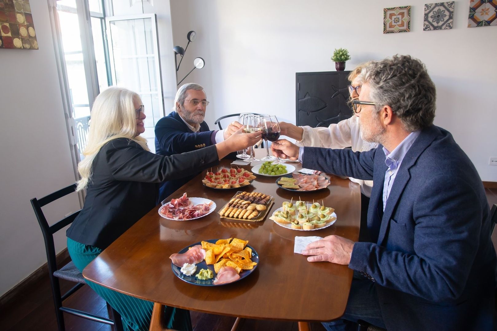 Fire venner skåler med vin ved et bord fyldt med tapas